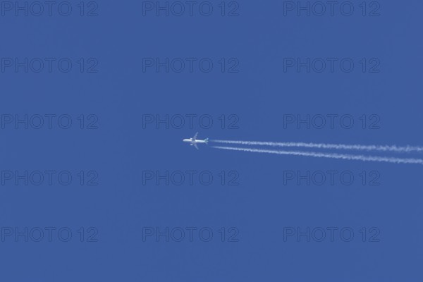 Jet passenger aircraft in flight in a blue sky with vapour trails or contrails behind, England, United Kingdom