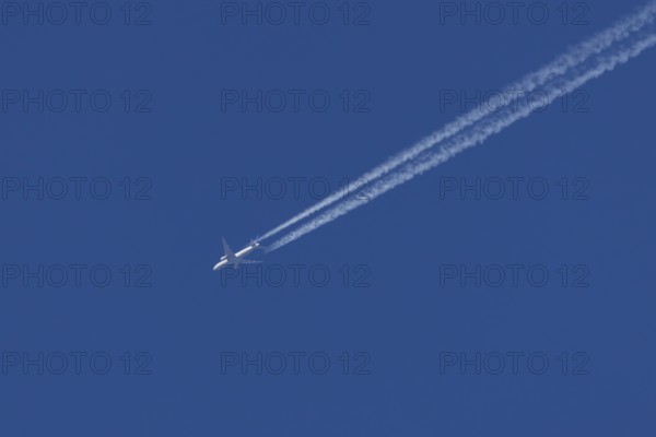 Jet passenger aircraft in flight in a blue sky with vapour trails or contrails behind, England, United Kingdom