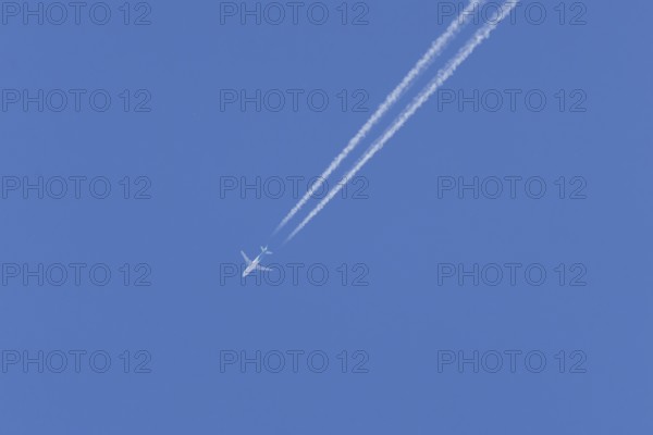Jet passenger aircraft in flight in a blue sky with vapour trails or contrails behind, England, United Kingdom