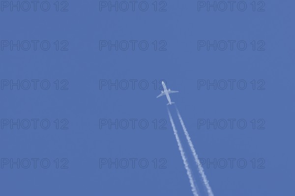 Jet passenger aircraft in flight in a blue sky with vapour trails or contrails behind, England, United Kingdom