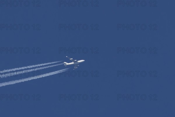 Boeing 747 Jumbo jet passenger aircraft in flight in a blue sky with vapour trails or contrails behind, England, United Kingdom