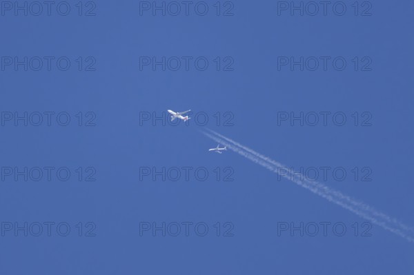 Two jet passenger aircraft in flight in a blue sky with vapour trails or contrails behind, England, United Kingdom