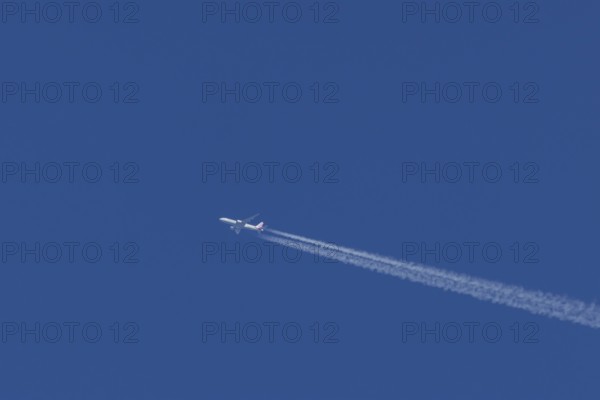 Jet passenger aircraft of American airlines in flight in a blue sky with vapour trails or contrails behind, England, United Kingdom