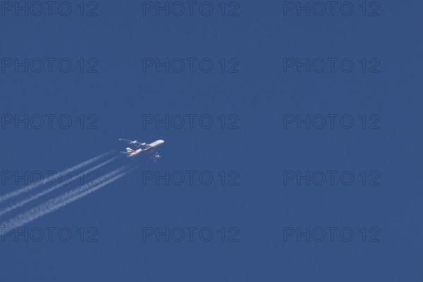 Airbus A380 jet passenger aircraft of Emirates airlines in flight in a blue sky with vapour trails or contrails behind, England, United Kingdom