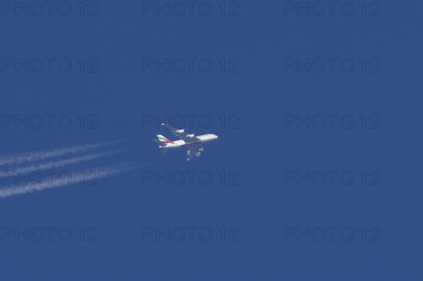 Airbus A380 jet passenger aircraft of Emirates airlines in flight in a blue sky with vapour trails or contrails behind, England, United Kingdom