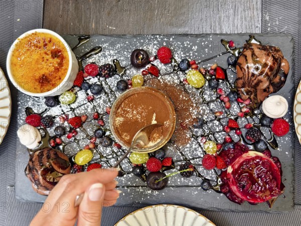 Hand with spoon tasting a dessert, surrounded by artfully arranged berries and chocolate Lower Austria Austria