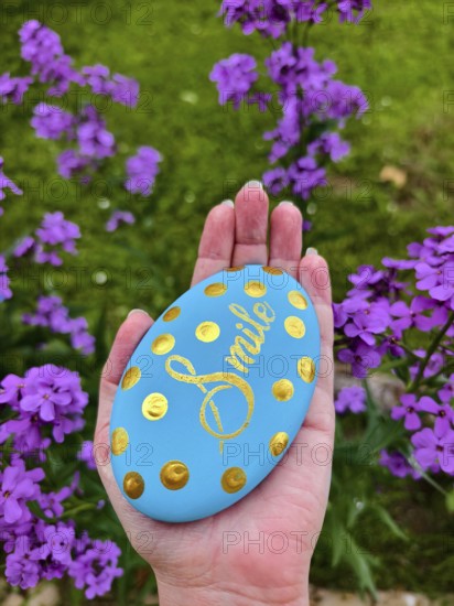 Hand holding blue stone with gold lettering and dots, purple flowers in the background Lower Austria Austria