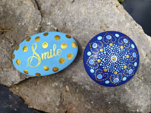 Two painted stones on rocks, one with 'Smile', one with a mandala pattern in blue and gold Lower Austria Austria