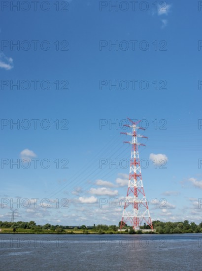 An extremely high electricity electricity electricity pylon, marked white and red, stands on the banks of the Elbe, river bank, Elbe crossing 2, 227 m high, highest overhead line pylon in Europe, surrounded by green landscape with trees and meadows under a blue sky, high-voltage pylon, overhead line pylon, overhead line, colour marking, safety, aviation safety, technology, structure, near Hollern-Twielenfleth, Lühe, Altes Land, Lower Saxony, Germany