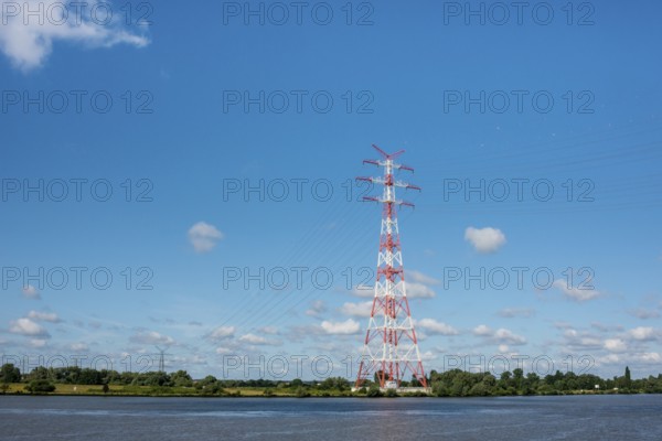 An extremely high electricity electricity electricity pylon, marked white and red, stands on the banks of the Elbe, river bank, Elbe crossing 2, 227 m high, highest overhead line pylon in Europe, surrounded by green landscape with trees and meadows under a blue sky, high-voltage pylon, overhead line pylon, overhead line, colour marking, safety, aviation safety, technology, structure, near Hollern-Twielenfleth, Lühe, Altes Land, Lower Saxony, Germany