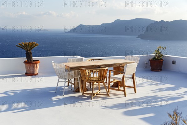 Wooden table and various chairs on a white terrace by the sea, view of the caldera, Oia, Santorini, Cyclades, Aegean Sea, Greece