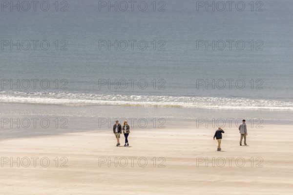Group of people walking in the sunshine on a sandy beach with rolling waves at the sea, Crozon peninsula, Bretagne, France