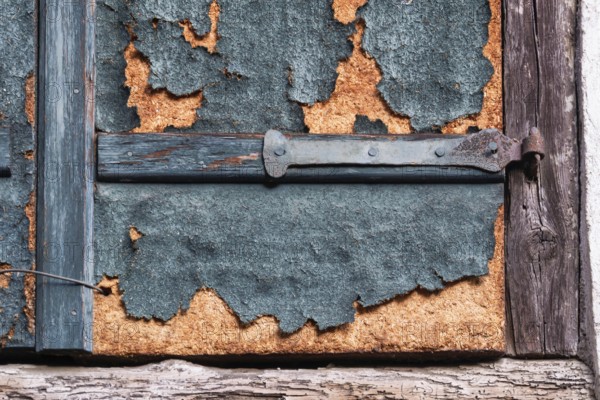 Weathered detail of an old shutter with rusty hinge and peeling paint, Alsace, France