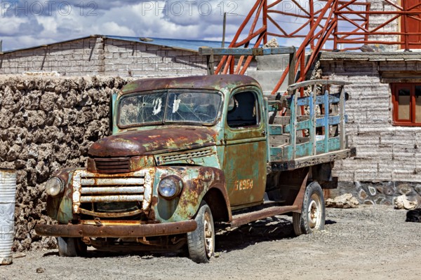 Rusty historic lorry next to an old brick building with outside stairs under a blue sky, Old lorry in a village on the edge of the Salar de Uyuni in Bolivia