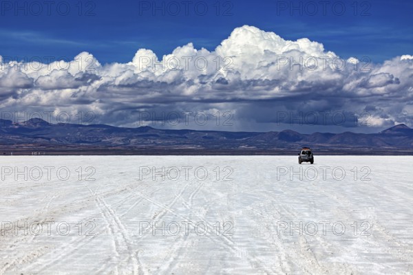 An off-road vehicle drives across an endless salt flat under a sky full of clouds, The endless expanses of the salt plain of the Salar de Uyuni in Bolivia