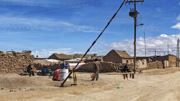 Small desert town with clay-like houses under a blue sky, power lines and local people, A village on the Altiplano plateau in Bolivia