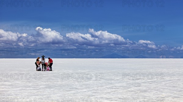 Group of people around a table on a vast white salt flat under a blue sky, The endless expanses of the salt plain of the Salar de Uyuni in Bolivia