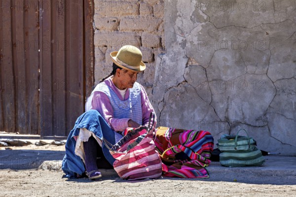 Man in traditional dress sits on the floor and sorts colourful bags on a wall, Traditional woman in a village in the Salar de Uyuni in Bolivia