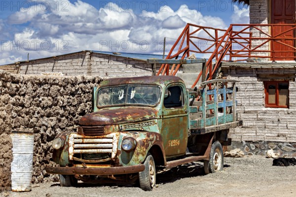 Rusty old lorry in front of a rustic building in a desert environment with blue sky and clouds, Old lorry in a village on the edge of the Salar de Uyuni in Bolivia