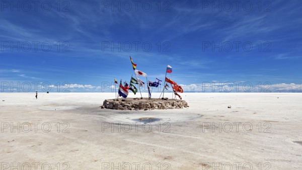 Flags in a vast salt lake under a clear blue sky with scattered clouds, international flags in the vastness of the salt plain of the Salar de Uyuni in Bolivia