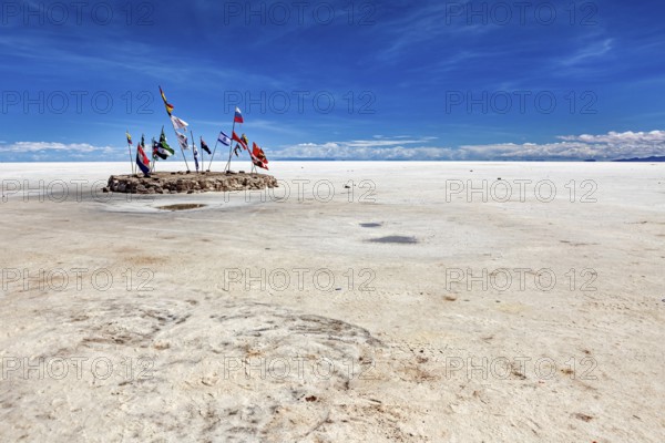 Flags in a vast salt lake under a clear blue sky with scattered clouds, international flags in the vastness of the salt plain of the Salar de Uyuni in Bolivia