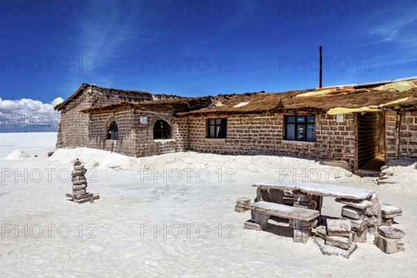 Rustic stone house in a desert-like landscape with blue sky and white ground, the salt hotel in the salt plain of the Salar de Uyuni in Bolivia