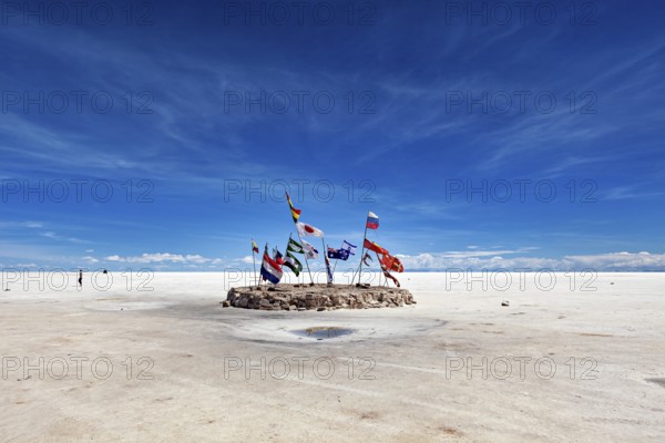 Flags in a vast salt lake under a clear blue sky with scattered clouds, international flags in the vastness of the salt plain of the Salar de Uyuni in Bolivia