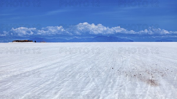 Vast salt flat with a mountain range on the horizon and clouds under a clear sky, The endless expanses of the Salar de Uyuni salt flat in Bolivia