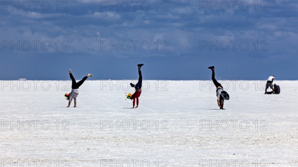 People doing handstands on a vast salt flat under a dramatic sky, The endless expanses of the salt plain of the Salar de Uyuni in Bolivia