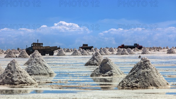 Lorries and salt hills on a reflective salt flat under a blue sky and clouds, The endless expanses of the salt plain of the Salar de Uyuni in Bolivia