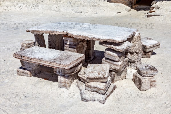 Rustic stone table with benches outdoors on a sandy, white surface, The salt hotel in the salt plain of the Salar de Uyuni in Bolivia