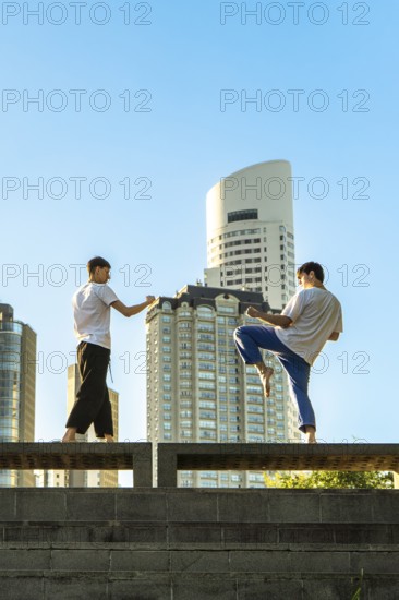 Vertical shot of two young men performing martial arts forms in a city setting