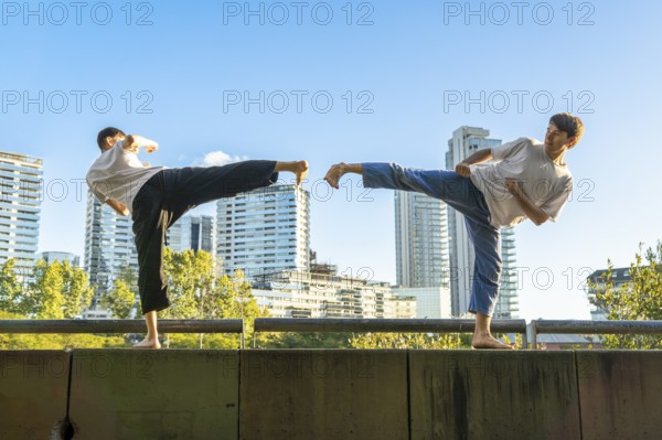 Young men executing synchronized Taekwondo kicks with urban buildings in the background