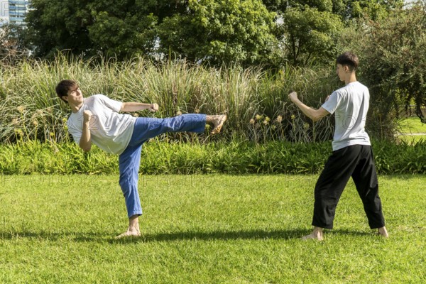 Young men practicing a taekwondo kick outdoors