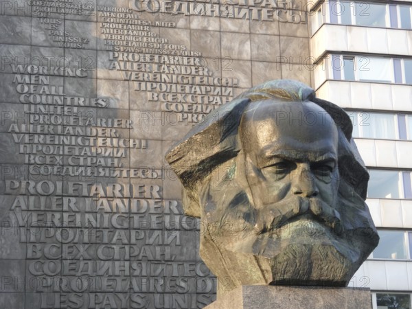 Stone bust of Karl Marx in front of a building with multilingual communist writings, Karl Marx monument in the city centre of Chemnitz, Saxony