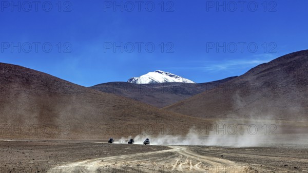 Vehicles drive through a dusty desert landscape with mountain views under a clear sky, The landscape of the Altiplano in Bolivia