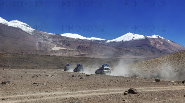 Off-road vehicle driving through a remote desert landscape with snow-capped mountains in the background, off-road in the landscape of the Altiplano in Bolivia