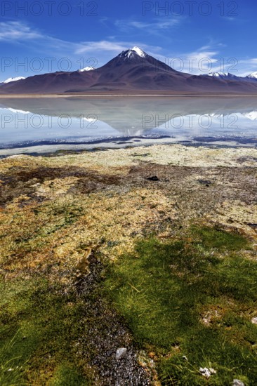 Volcano in front of a clear lake whose surface reflects the summit and the blue sky, The Laguna Colorada in Bolivia