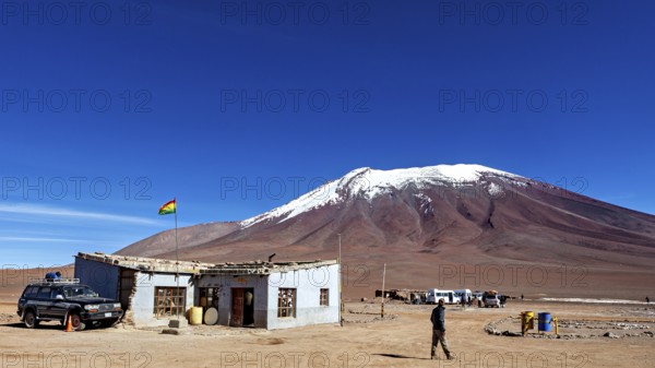 A remote mountain region with a simple building and a vehicle, overlooked by a clear blue sky, The border control between bolivia and Chile