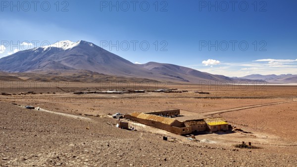 A small house stands in an arid desert landscape in front of an impressive mountain under a clear sky, The landscape of the Altiplano in Bolivia