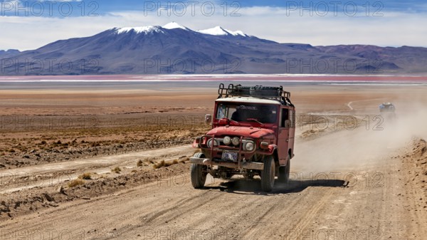 A jeep drives dusty on a desert road with mountains in the background, off road in the landscape of the Altiplano in Bolivia