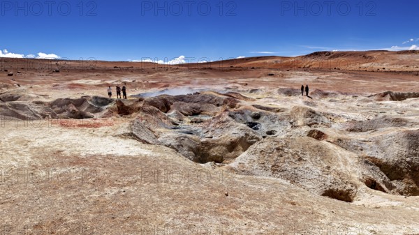 Landscape with geysers in a desert, two people on the horizon, clear blue sky, The mud volcanoes and fumaroles on the Altiplano in Bolivia