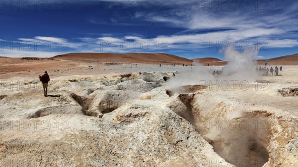 Lone hiker in a desert landscape with a smoking geyser and blue sky, The mud volcanoes and fumaroles on the Altiplano in Bolivia