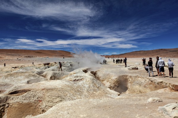 People standing in a desert landscape with a smoking geyser and blue sky, The mud volcanoes and fumaroles on the Altiplano in Bolivia