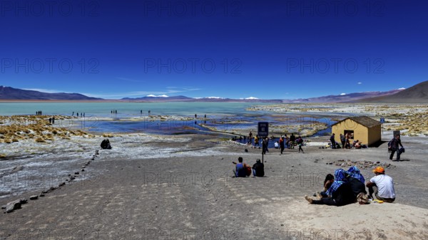People enjoy the view of a desert landscape with a disused building and a lake, The Aguas Termales de Polques in Bolivia