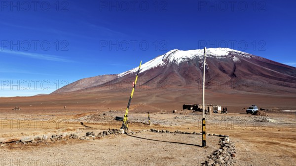 Border area in a treeless desert landscape with a snow-capped mountain and clear blue sky, The border control between bolivia and Chile