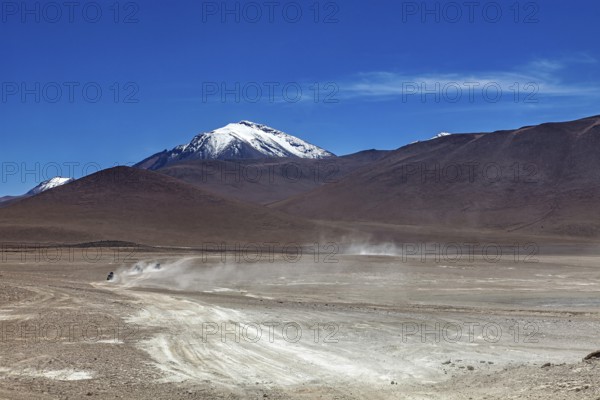 Vehicle tracks lead through a vast, dusty desert landscape to a snow-capped mountain, The landscape of the Altiplano in Bolivia