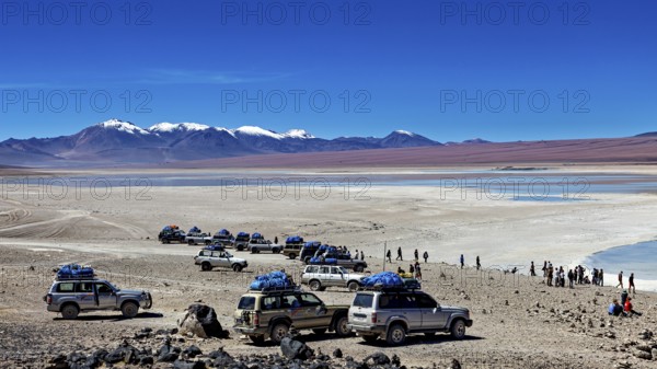 Several off-road vehicles parked in a desert landscape with mountains and snow-capped peaks under a clear sky, Off Road in the Landscape of the Altiplano in Bolivia