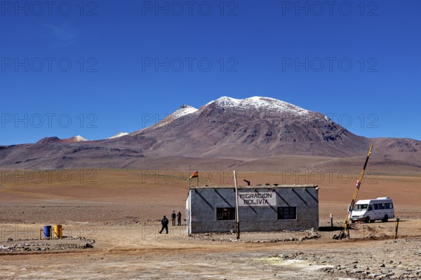 A small migration building in a vast desert landscape with snow-capped mountains, The border control between bolivia and Chile