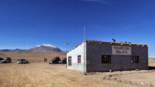 A small border building in a barren landscape with snow-capped mountains in the background, The border control between bolivia and Chile